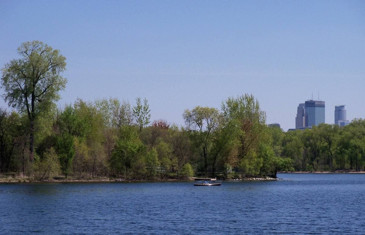 A blue lake edged with spring trees and the Minneapolis skyline in the distance