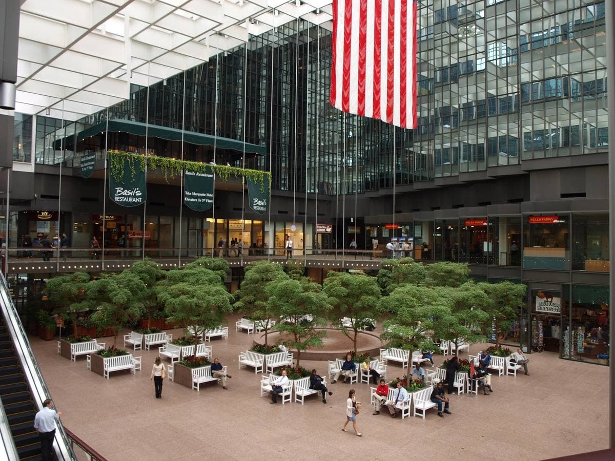 A glass-roofed atrium with trees, tables and an upper skyway level