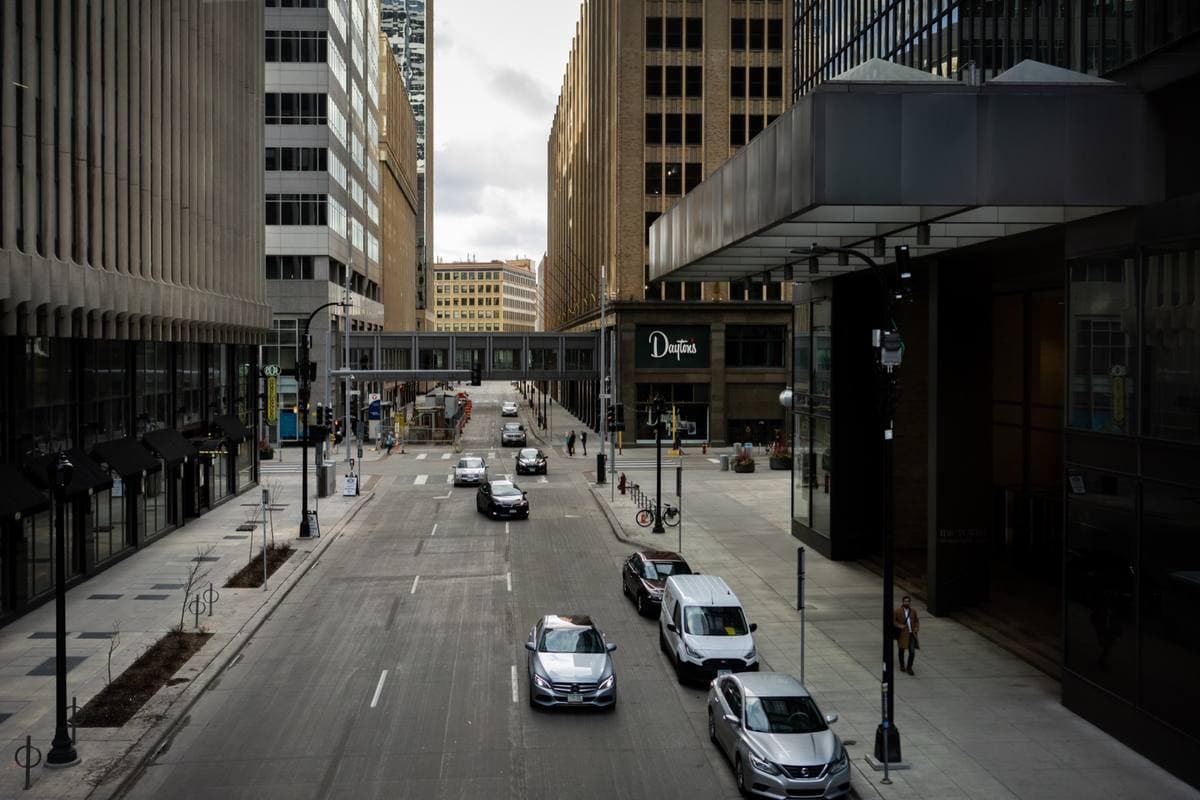 A downtown street between tall buildings, with a skyway bridge crossing it