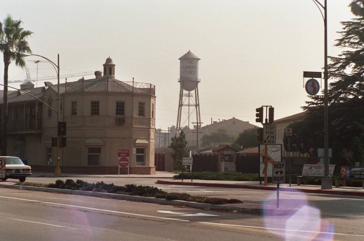 A studio building and a water tower behind a quiet road junction, in soft hazy light