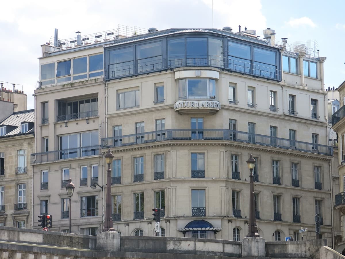 A tall stone building on the river bank with a restaurant glazed along its top floor