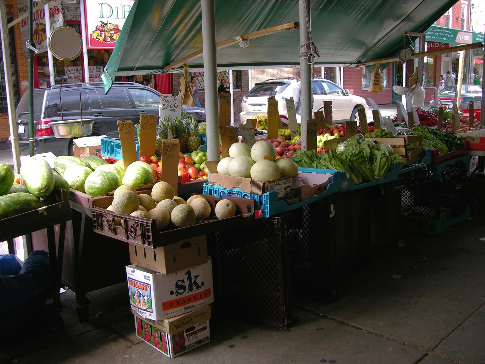 Melons, peppers and greens stacked on a market stall under a green awning