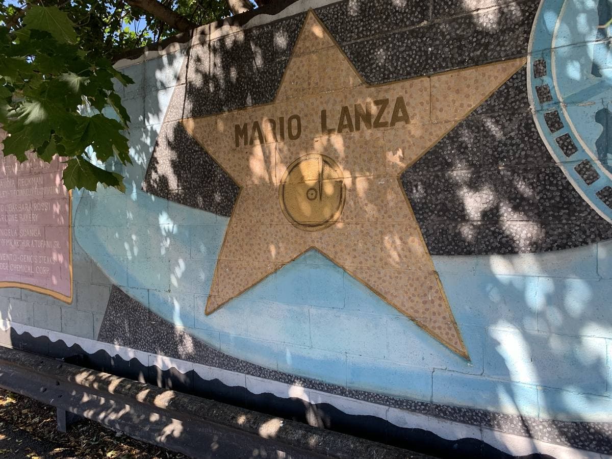 A mosaic star reading Mario Lanza set into a painted mural wall, in dappled shade