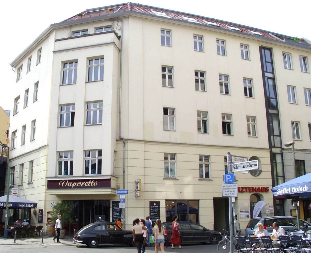 A pale corner building on Albrechtstraße with café tables and parked cars