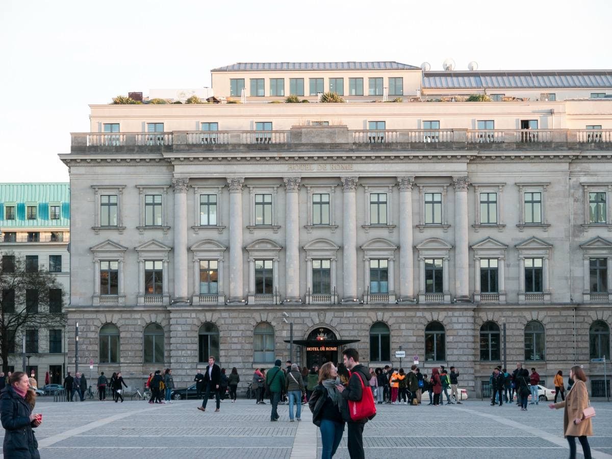 A long stone palace front on a paved square with people walking past