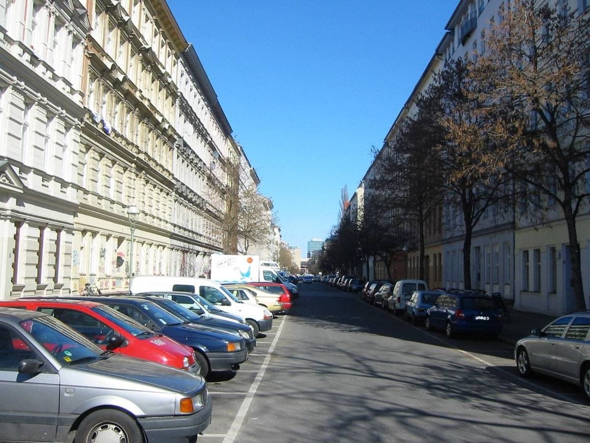A straight Kreuzberg street of old apartment houses with parked cars