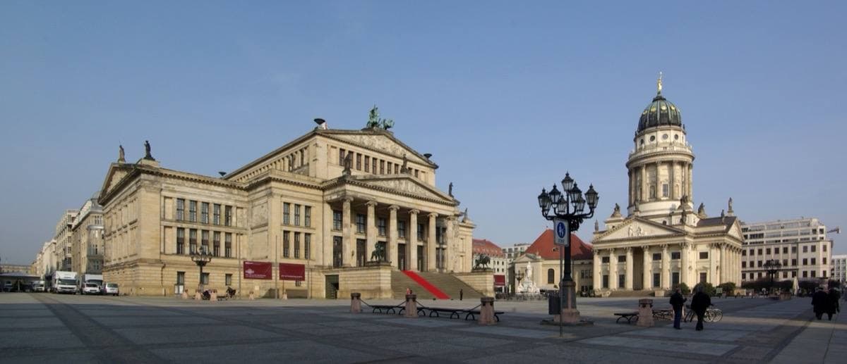 A wide paved square with a columned concert hall and a domed church