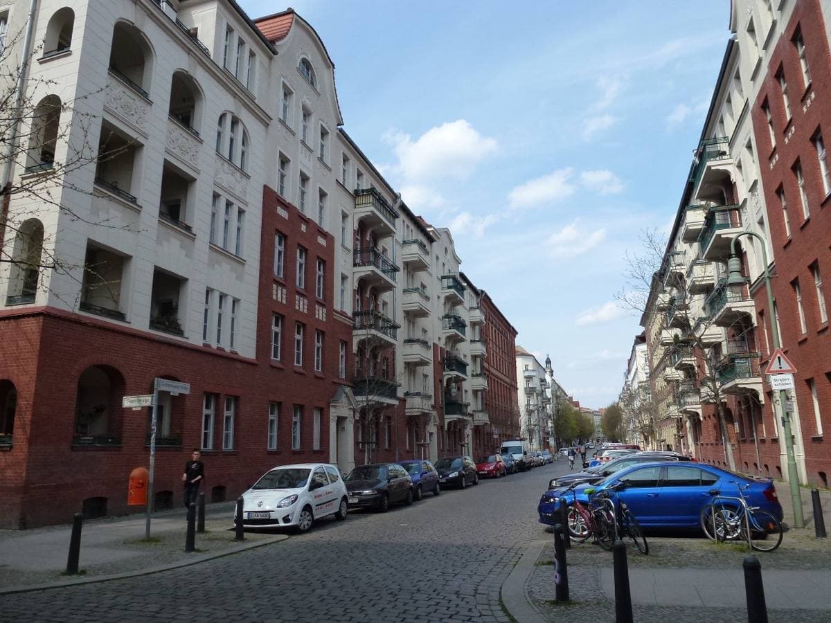 A cobbled side street of old apartment houses with parked cars