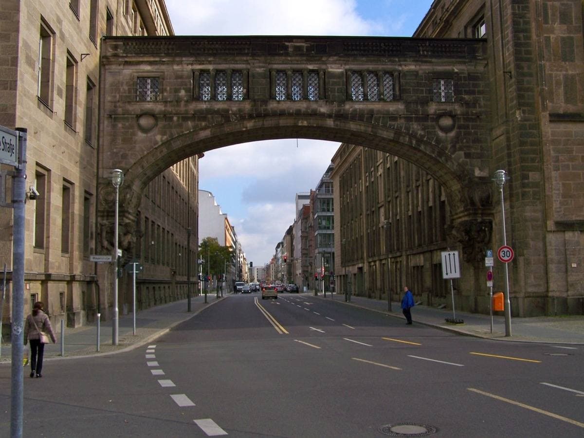 A stone bridge arching over Mauerstraße between two sandstone office blocks