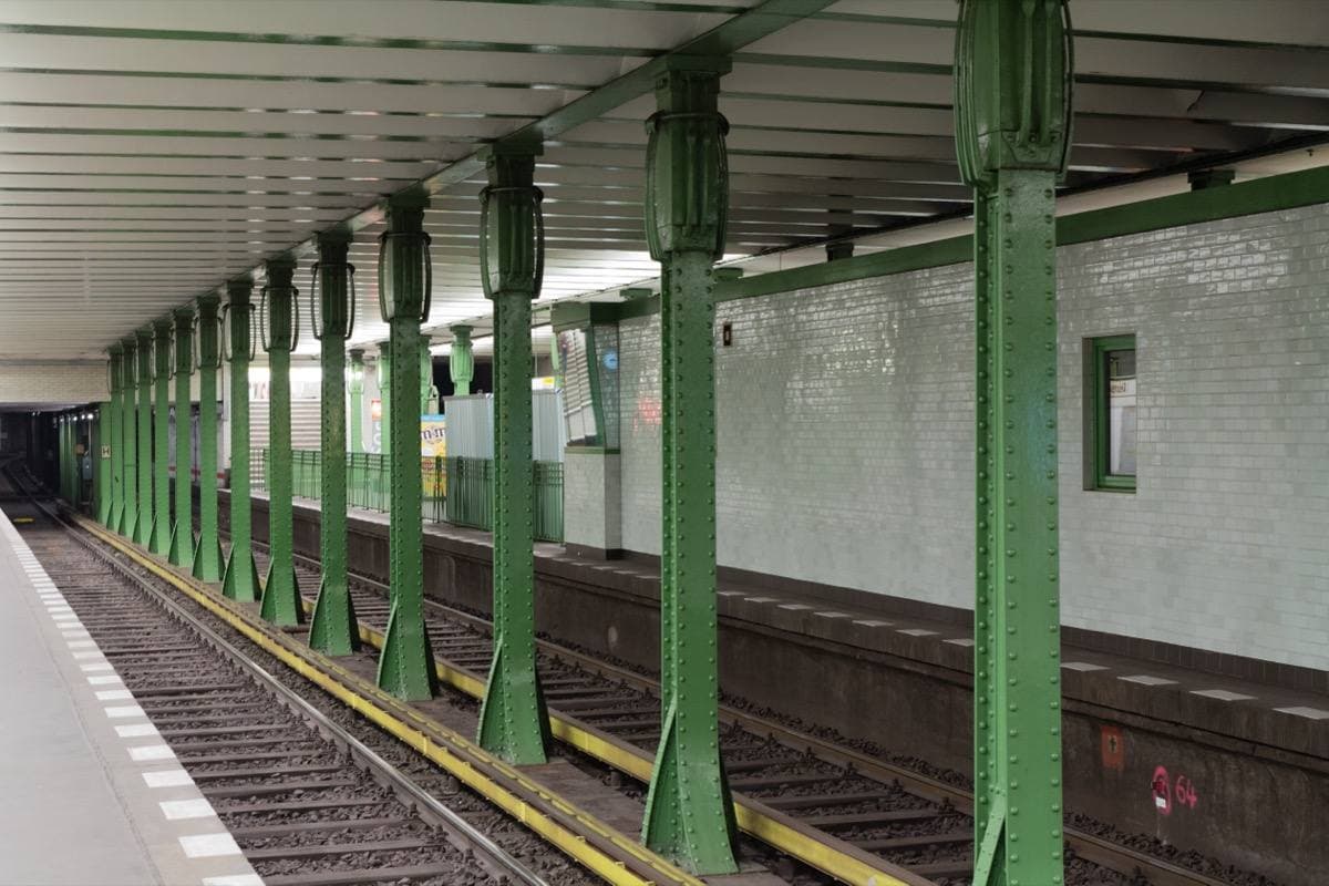 An underground platform with green iron columns and white tiles