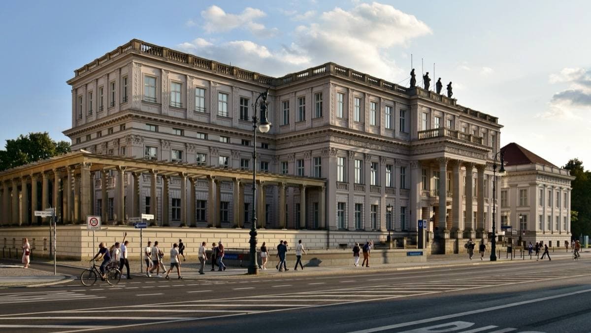 A pale neoclassical palace with a colonnade on a wide boulevard