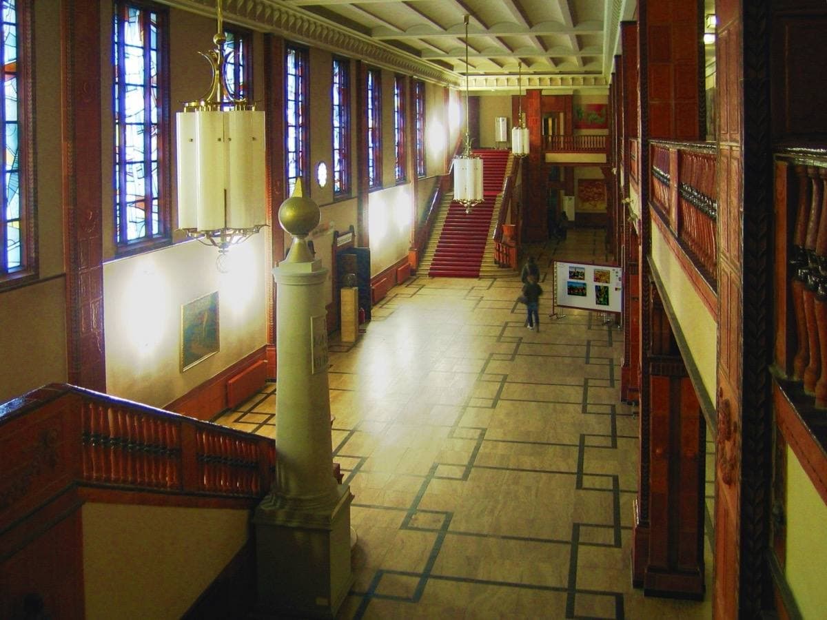 A long wood-panelled hall with a chequered stone floor and hanging lamps