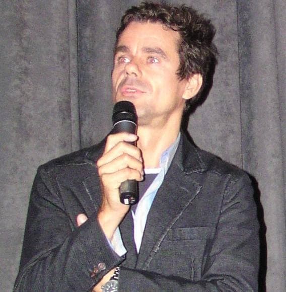 Tom Tykwer in a dark jacket, holding a microphone
