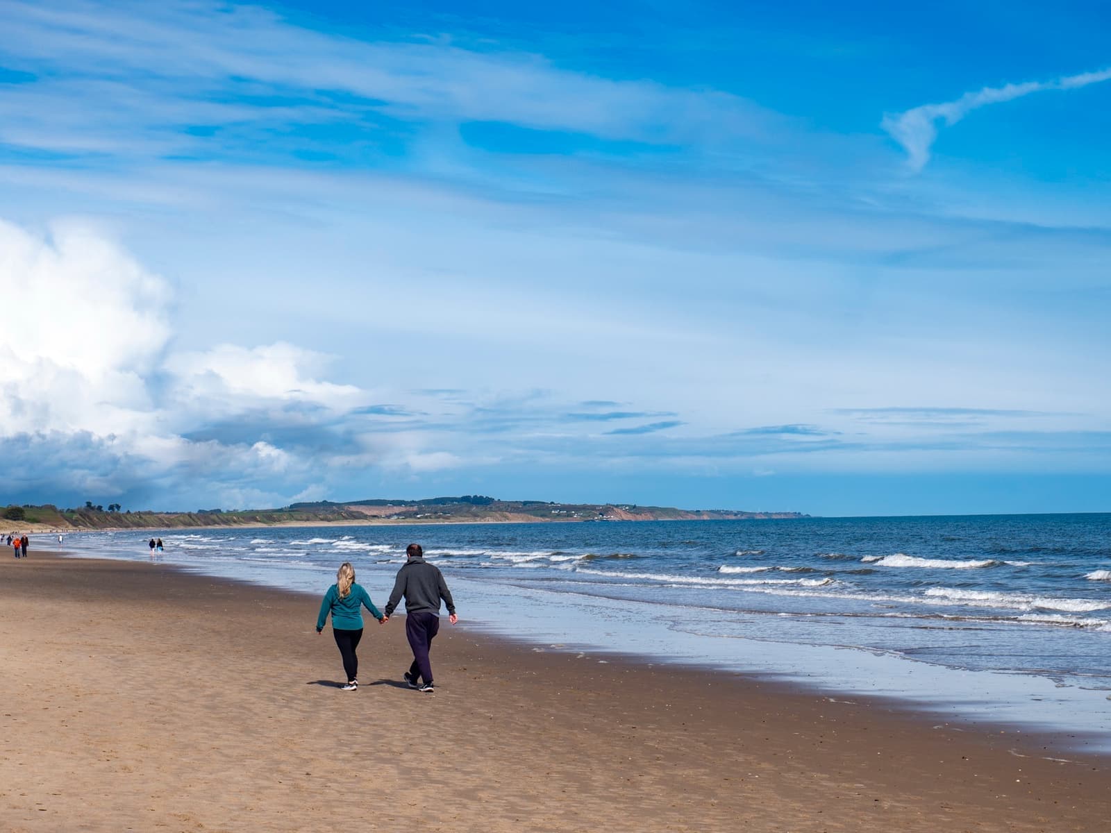 Two people walking at the water’s edge on a wide sandy beach