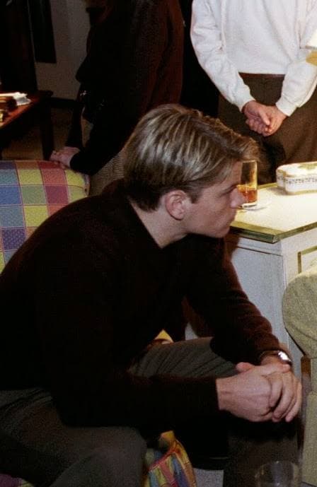 Matt Damon, in a dark sweater, sits forward on a checked sofa