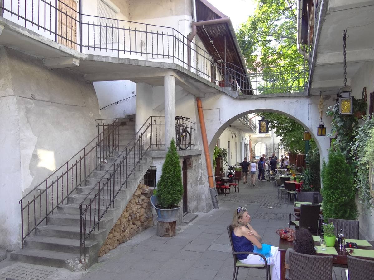 A narrow courtyard with an outside staircase, iron balconies and café tables