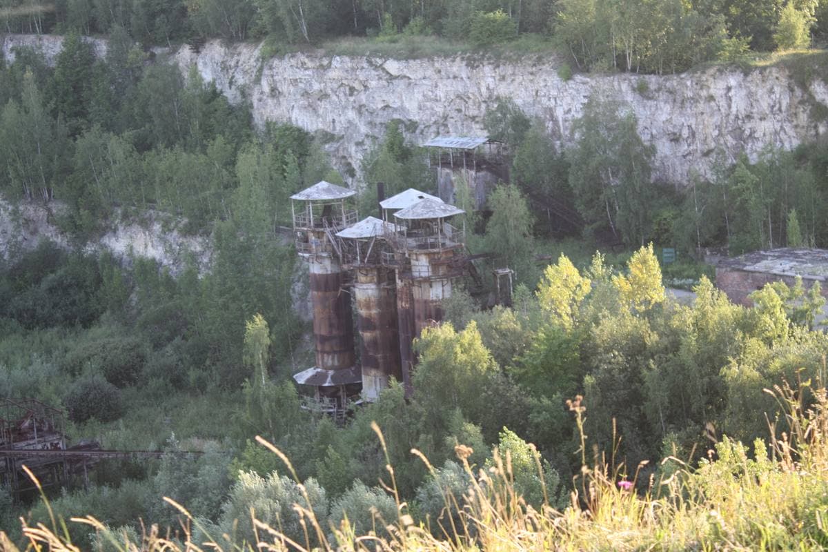 An overgrown quarry floor below a pale rock face, with old rusted towers