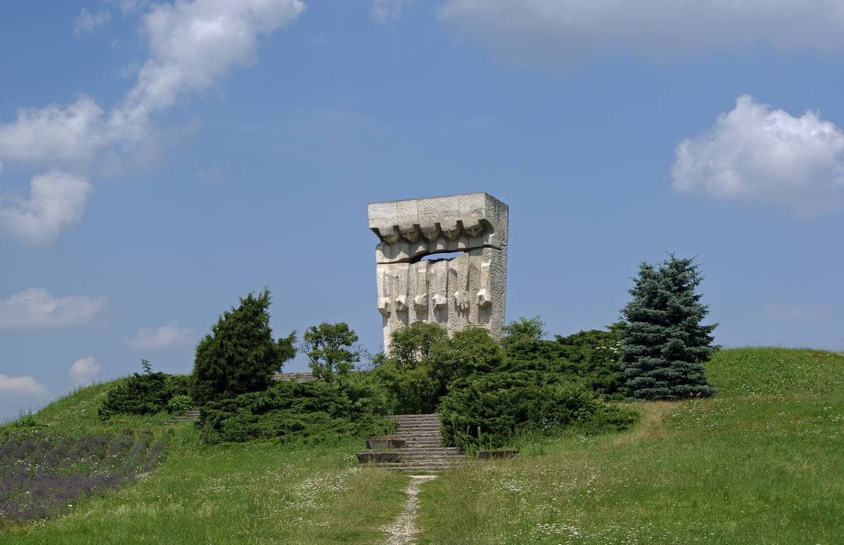 A stone monument of bowed figures on a grassy rise against the sky