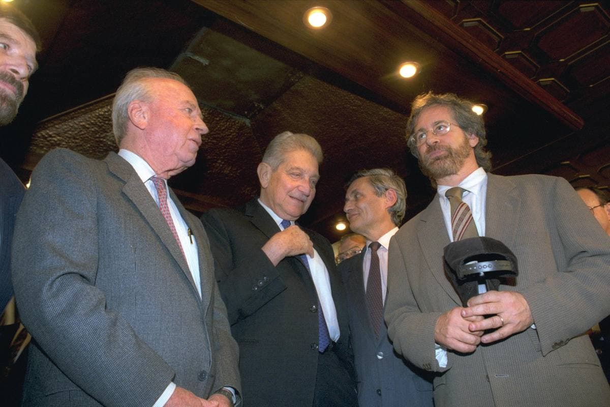 Three men in suits talking in a crowded foyer