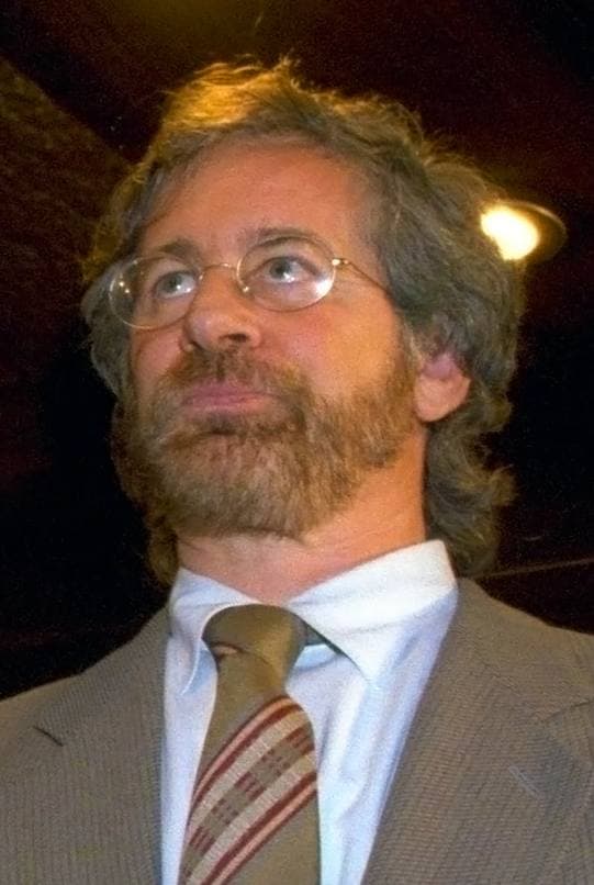 Steven Spielberg, bearded, in a suit and tie, looking up