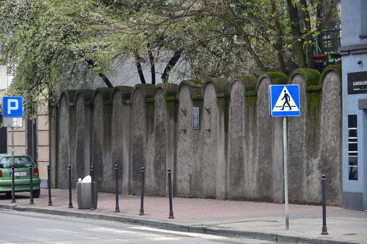 A long grey wall with arched tops beside a pavement