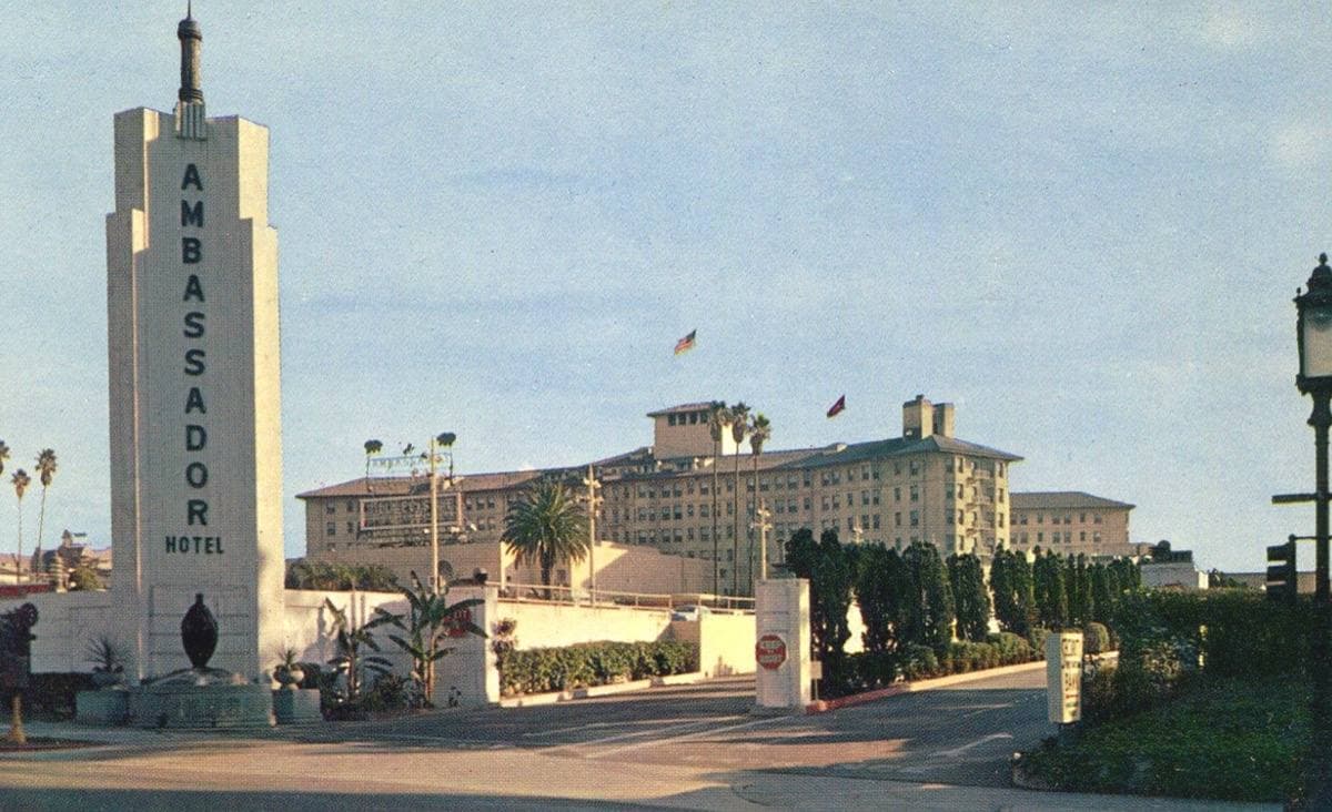 A postcard of a hotel entrance gate with palms and a lawn