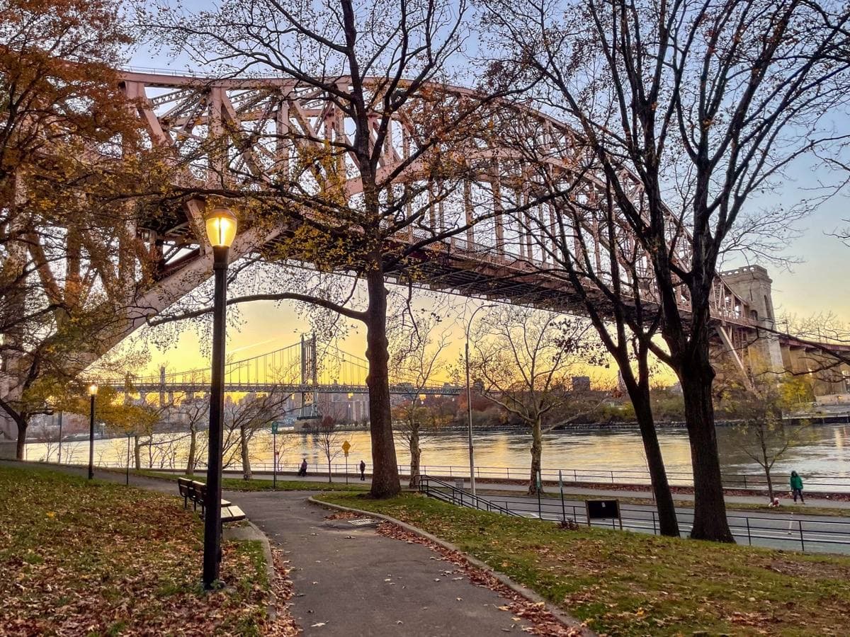 A steel arch bridge on stone towers over a park path