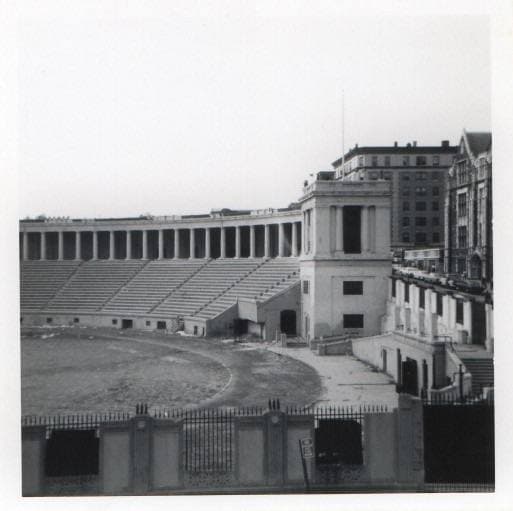 An empty stone amphitheatre with a colonnade, a college building behind