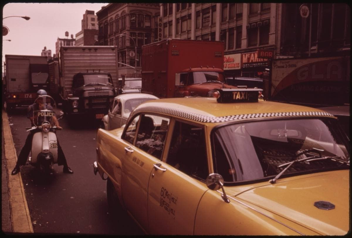 A yellow cab, a moped and lorries on a hazy Manhattan avenue
