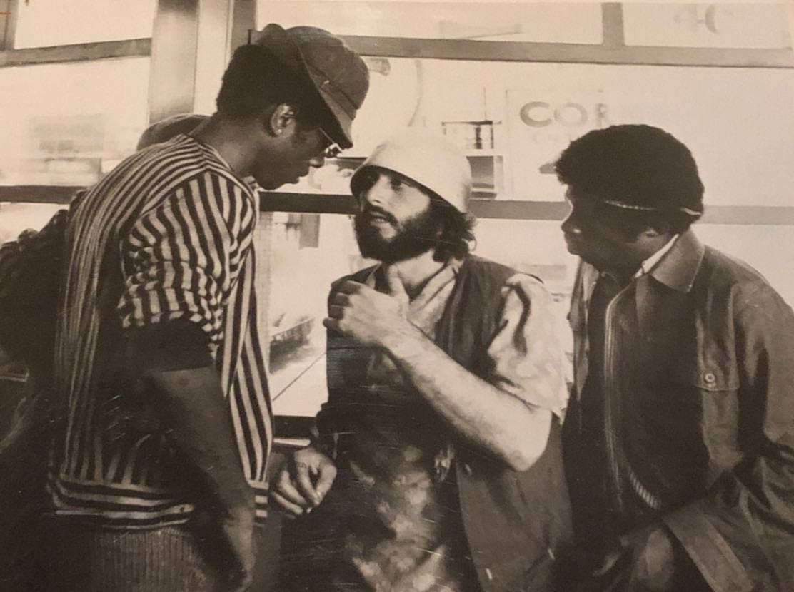 Al Pacino in a hard hat and a beard between two men in a doorway