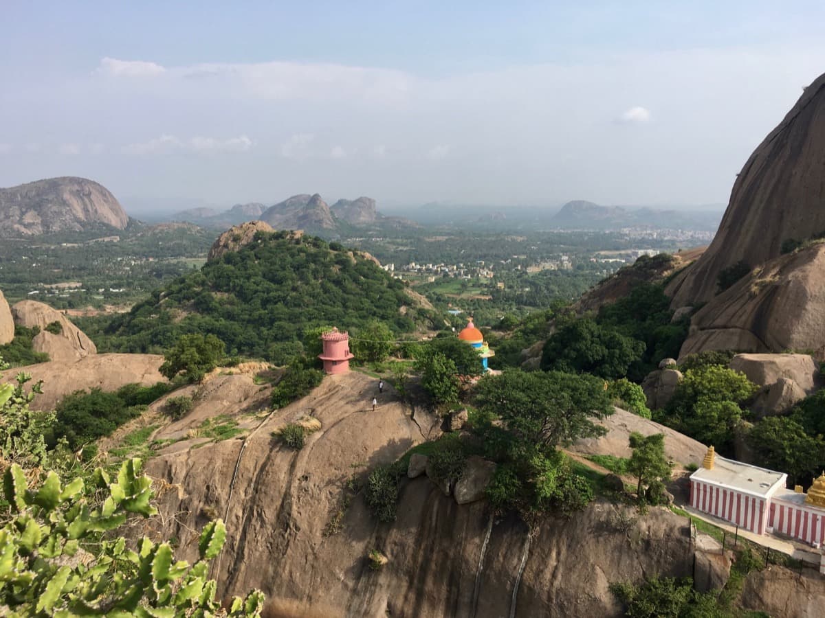 A view across bare granite slabs and small shrines to rocky hills in the distance