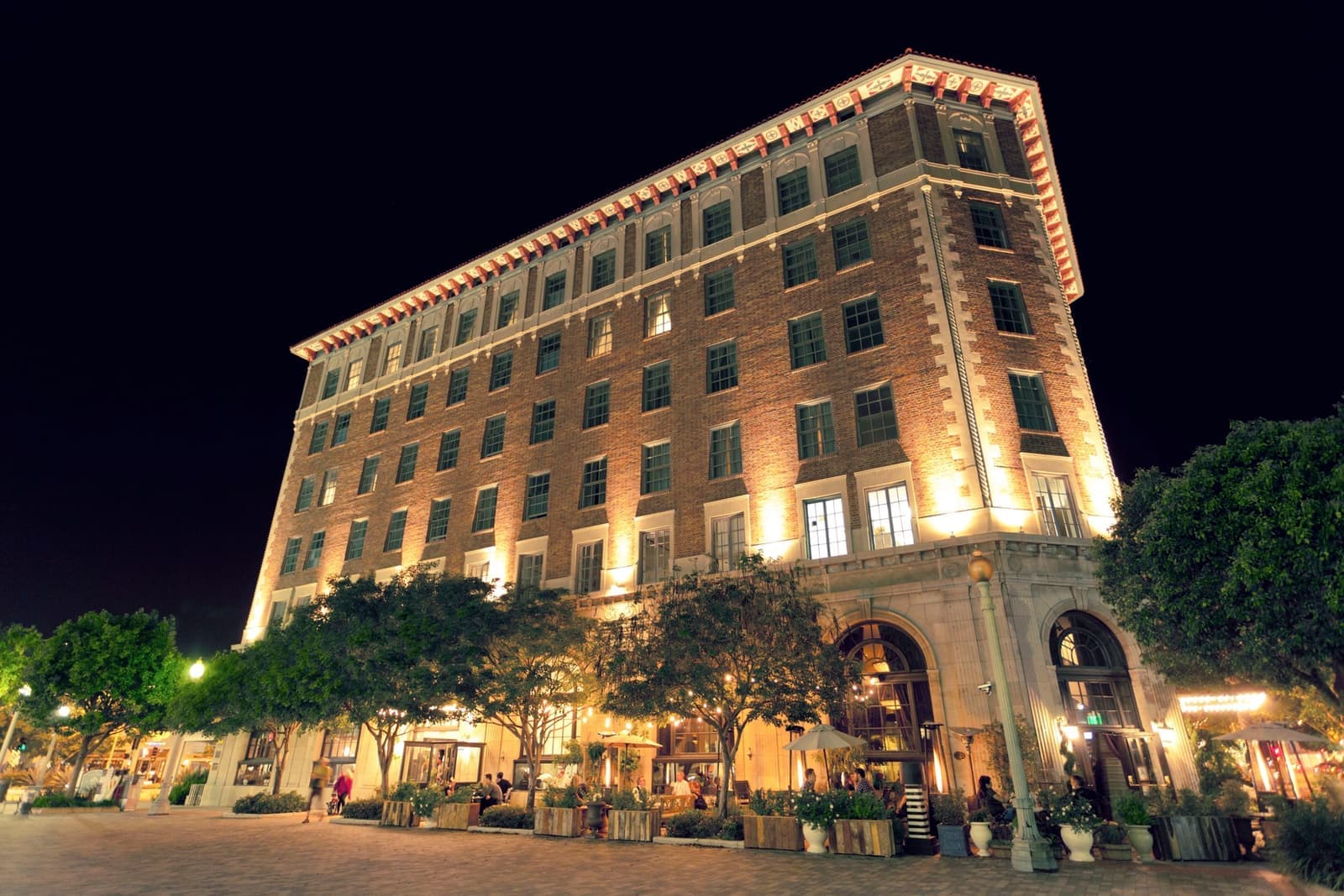A narrow wedge-shaped brick hotel lit up at dusk