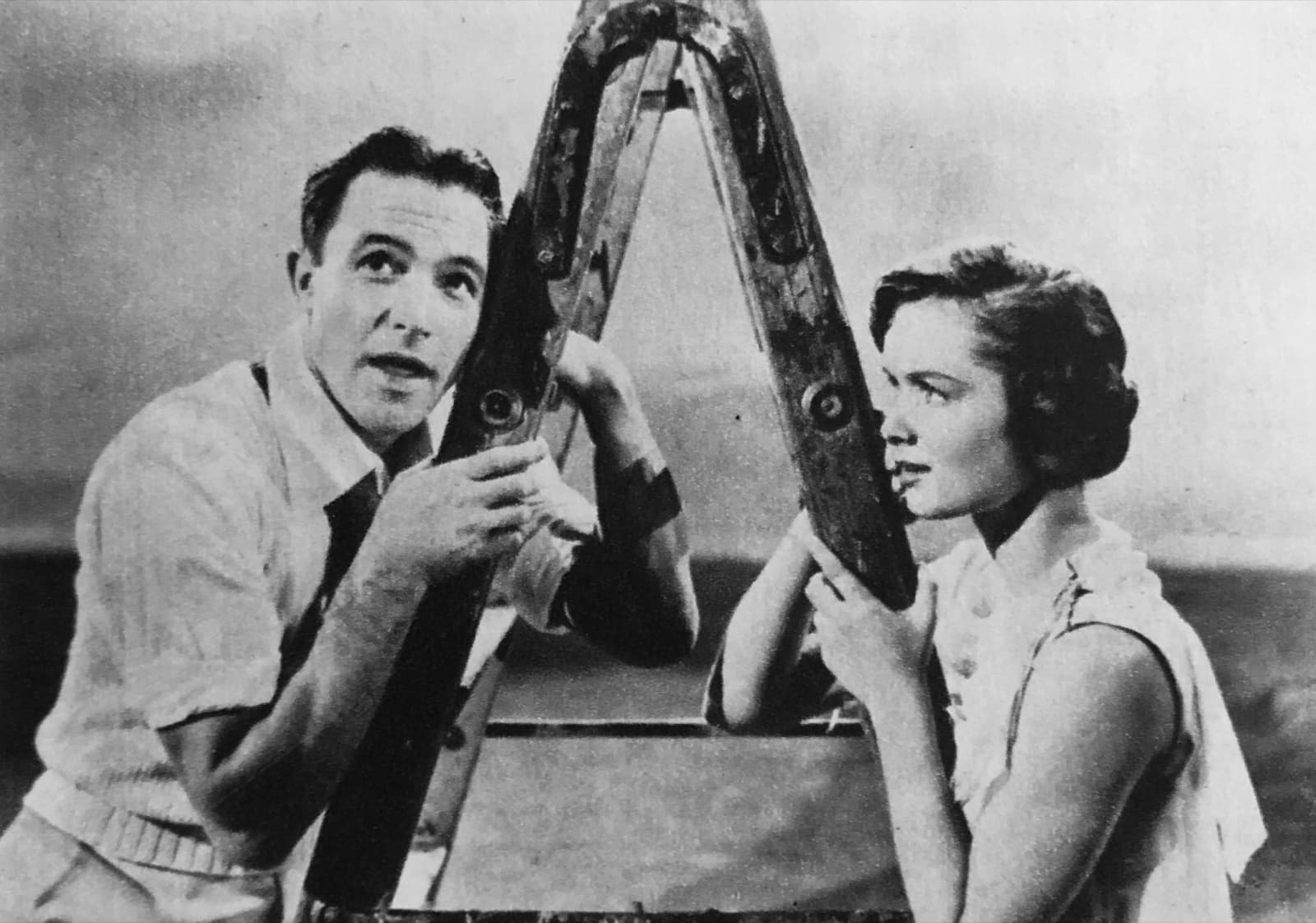 Gene Kelly and Debbie Reynolds lean on either side of a stepladder, looking up