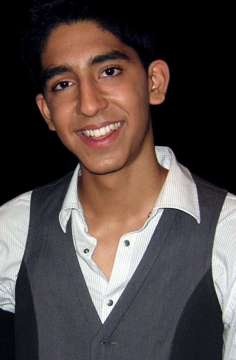 Colour photograph of a smiling young man in a grey waistcoat and striped shirt against a dark background