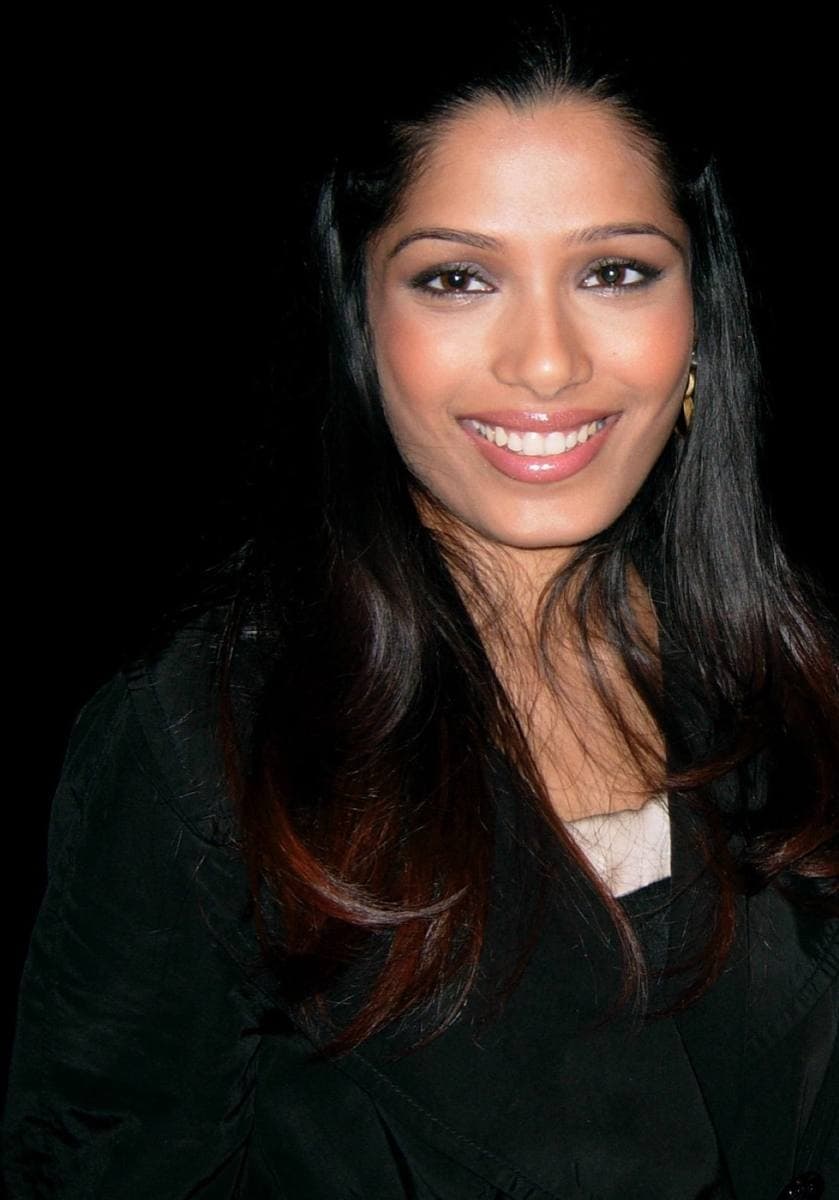 Colour photograph of Freida Pinto with long dark hair, smiling, against a black background