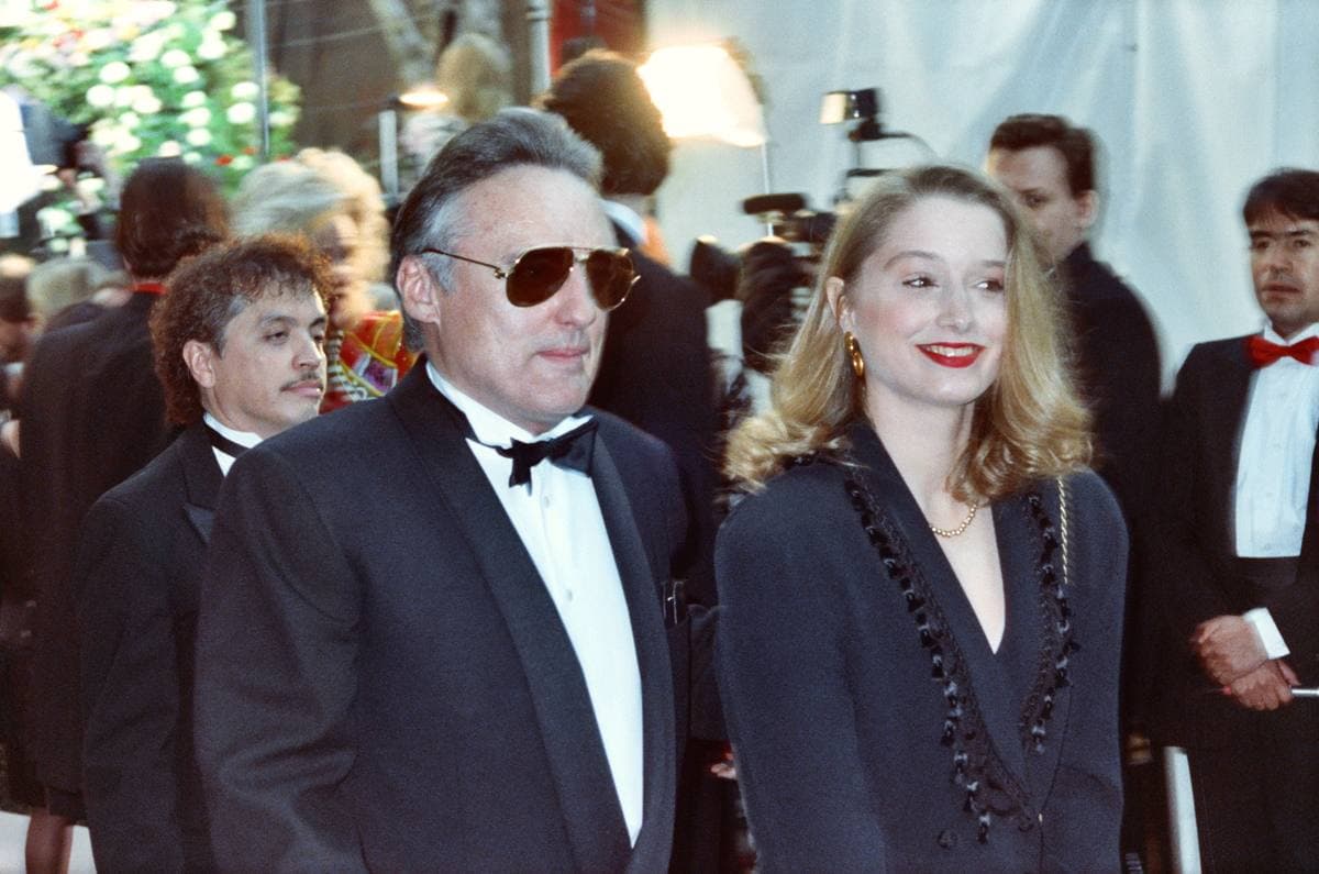 Dennis Hopper in a dinner jacket and dark glasses beside a woman in black at a crowded awards arrival