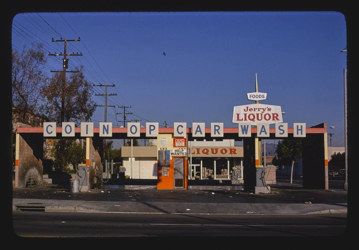 A coin-op car wash and liquor store sign on Main Street at dusk