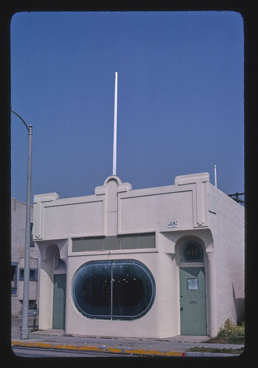 A small white stuccoed building with a round window on Rose Avenue under a blue sky