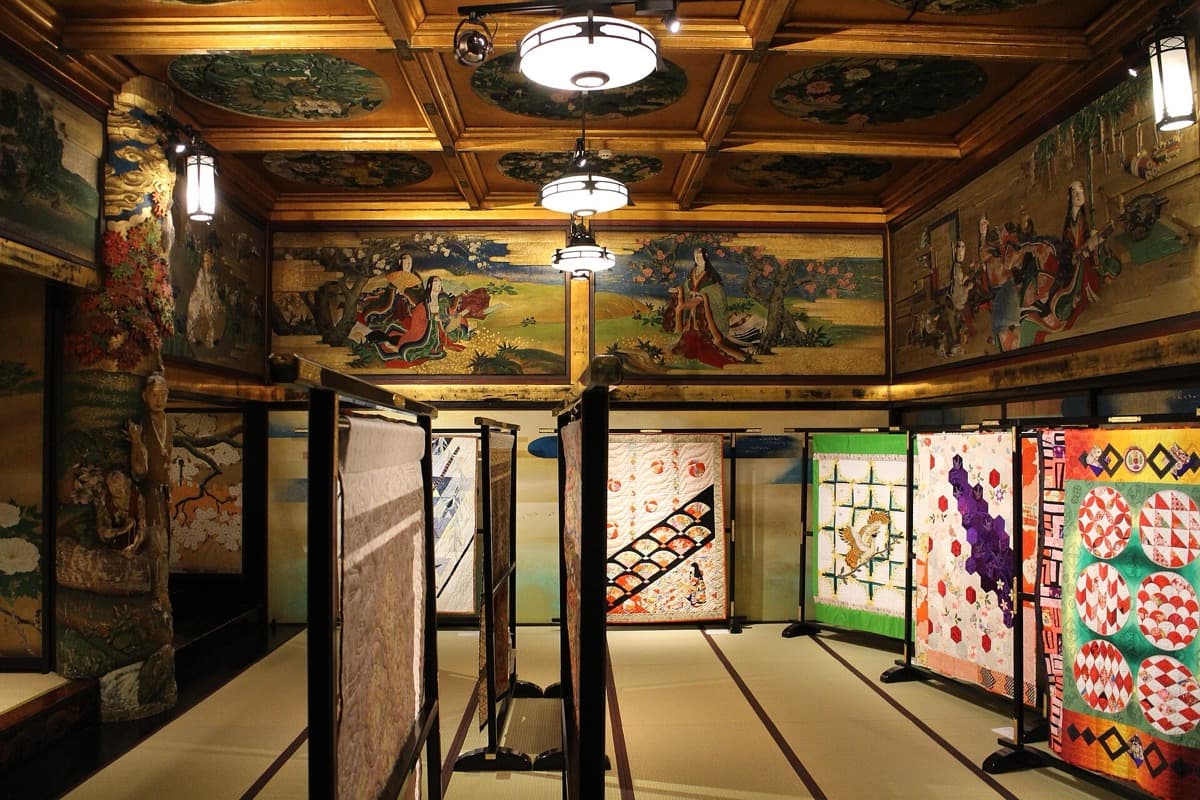 A tatami hall under a coffered ceiling with painted panels and gilded walls and folding screens