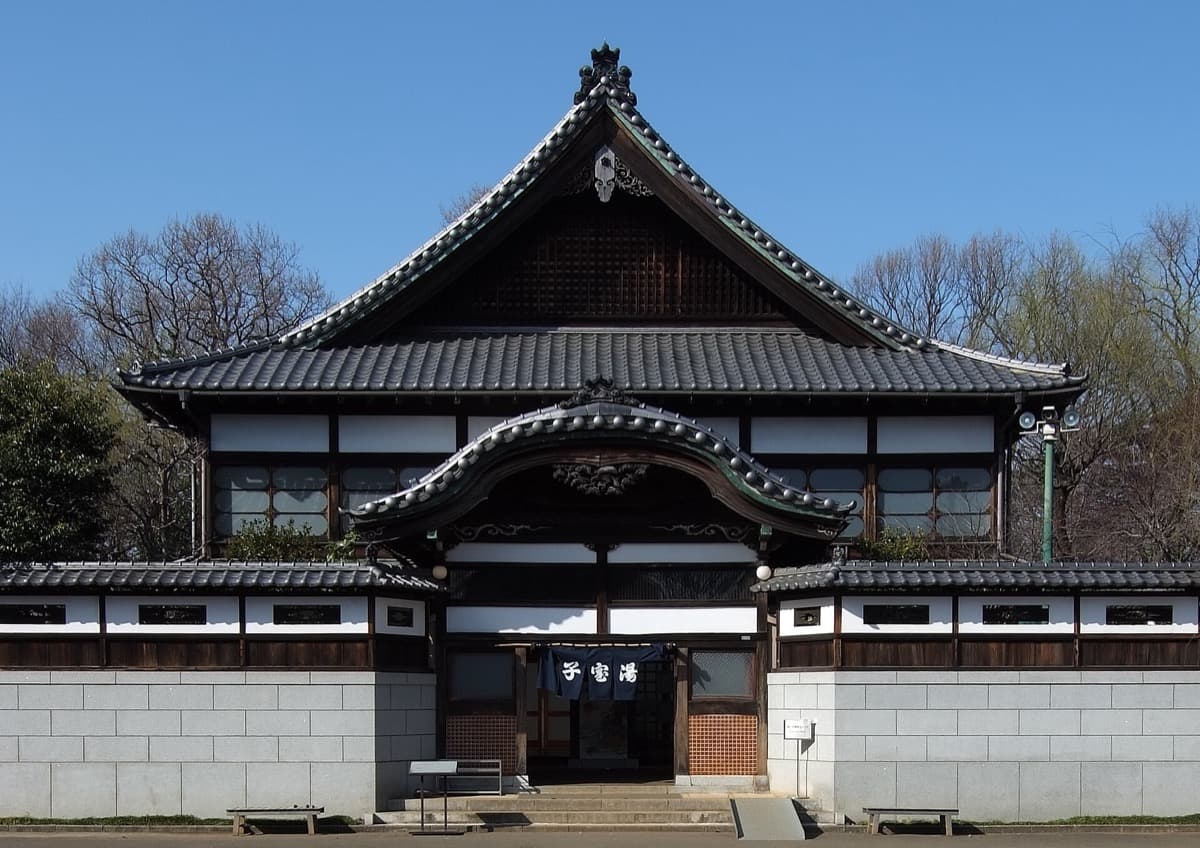 A bathhouse with a layered curved temple-style roof and white lower wall