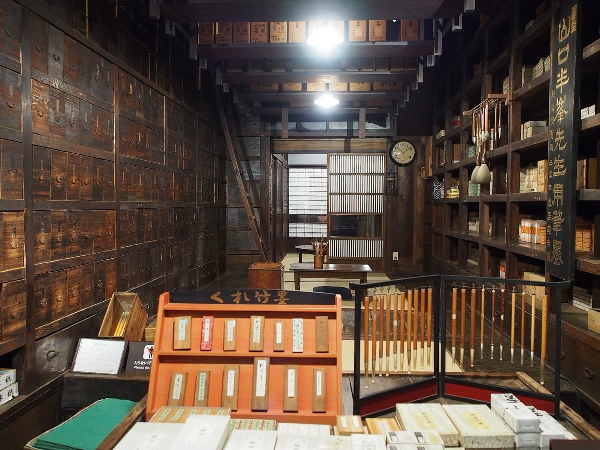 A wall of small wooden drawers beside shelves of stationery in a dim shop