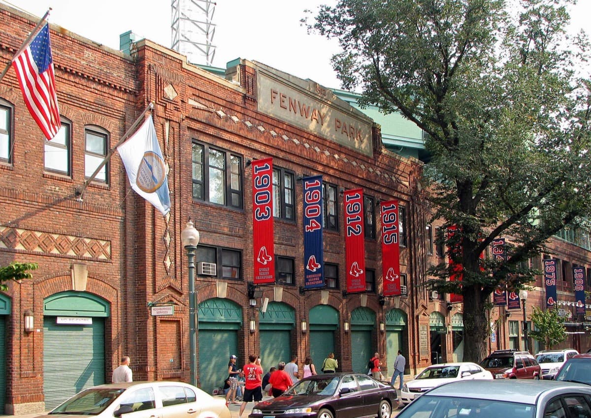 The brick front of a baseball ground with ticket windows and a street in front