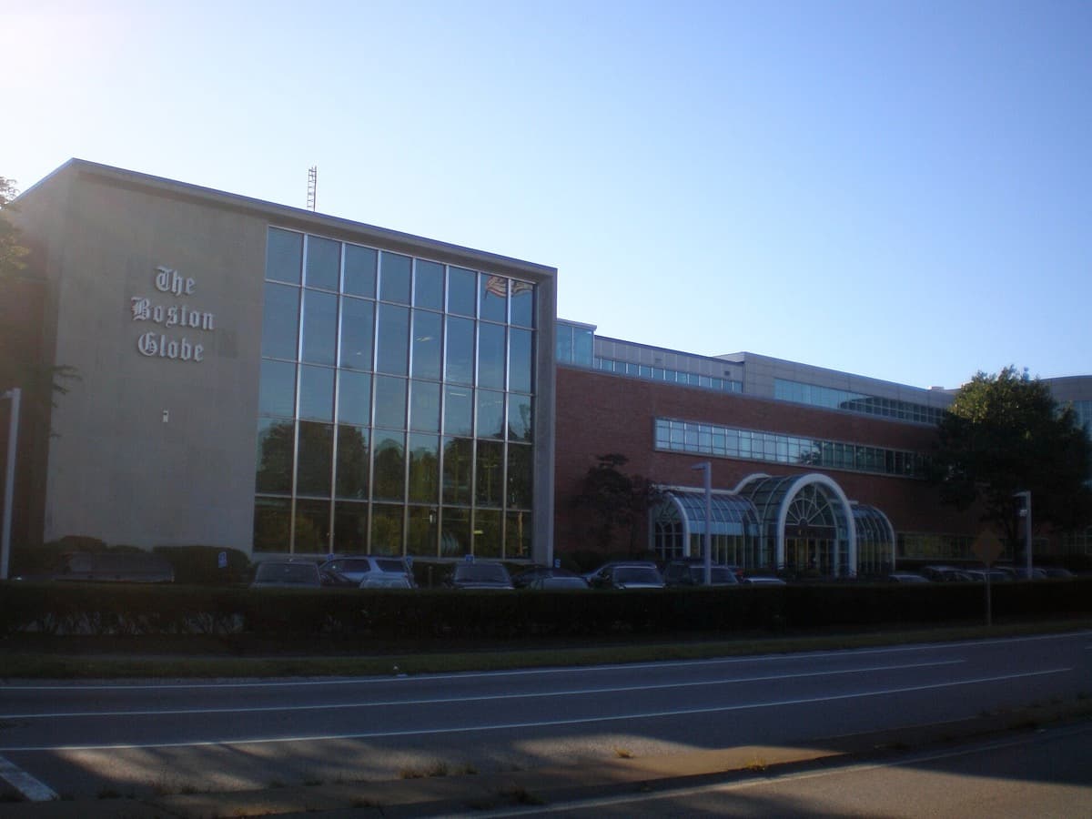 A low, wide office and printing-plant building beside a road, with a sign on its front