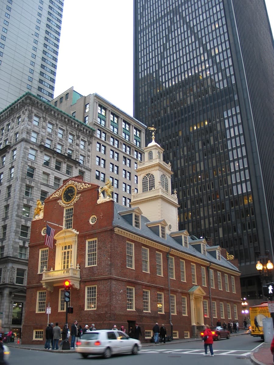 A narrow brick building with a stepped gable and a lion and unicorn on its top, among tall towers