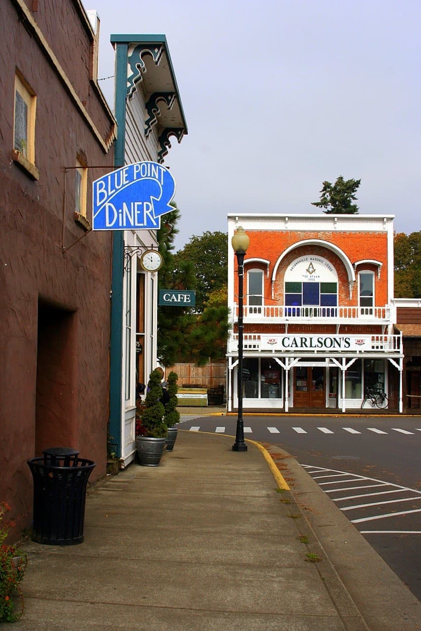 A blue sign reading Blue Point Diner hangs over a pavement, with Carlson’s at the end of the street