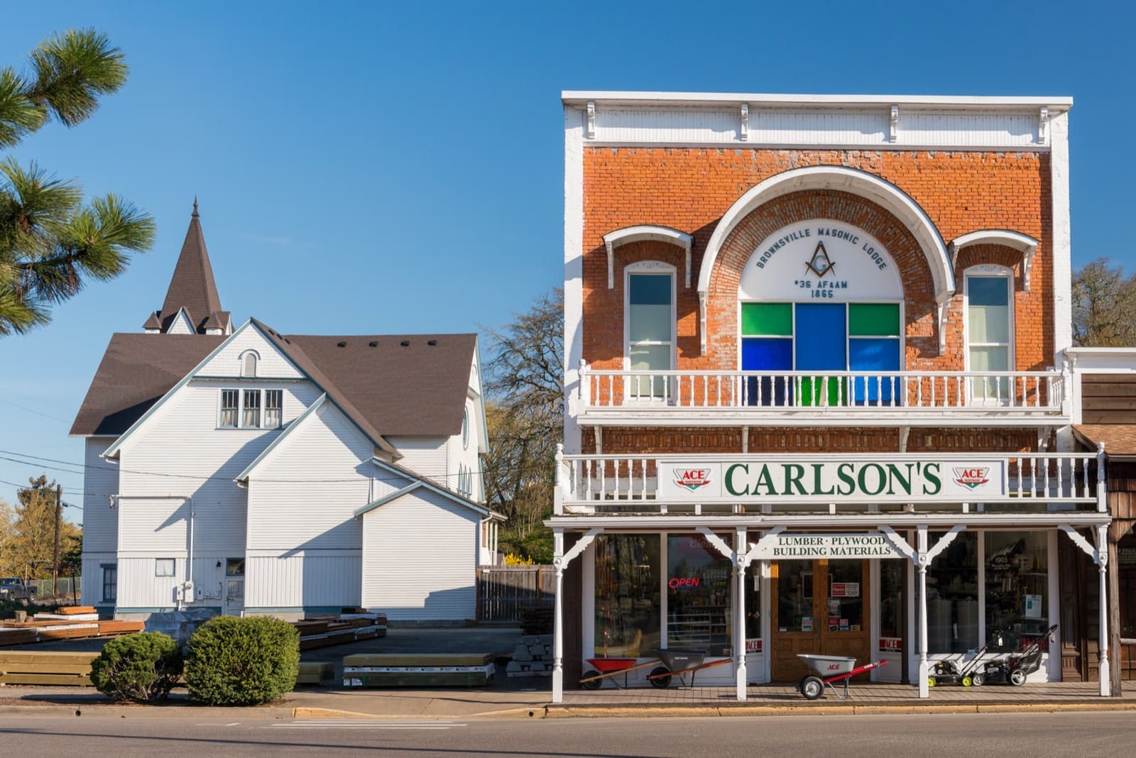 A red-brick building with white balconies and a CARLSON’S sign, a white church beside it, a striped crosswalk in the street