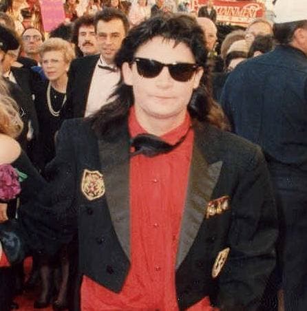 Corey Feldman in sunglasses, a red shirt and an embroidered black jacket
