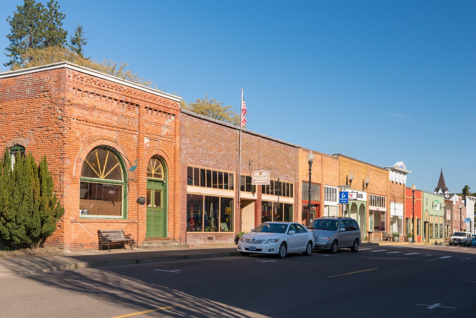 A row of brick and painted shopfronts along a quiet main street under a blue sky