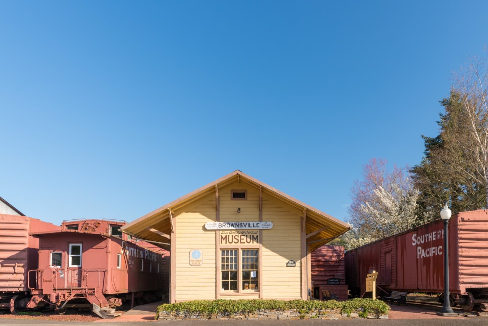 A pale yellow wooden depot with a MUSEUM sign, a red caboose and a Southern Pacific boxcar either side
