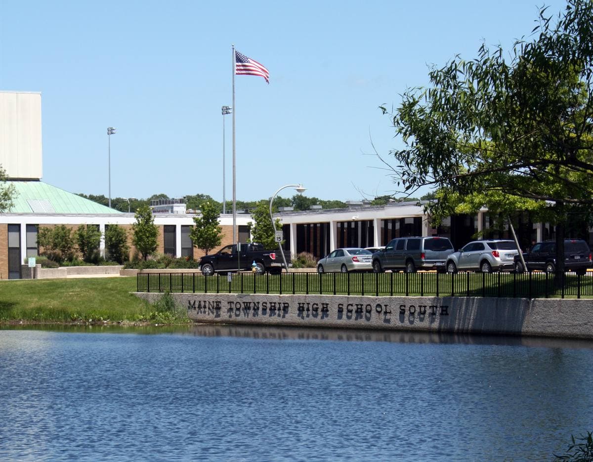 A low white school building with a flagpole beyond a pond